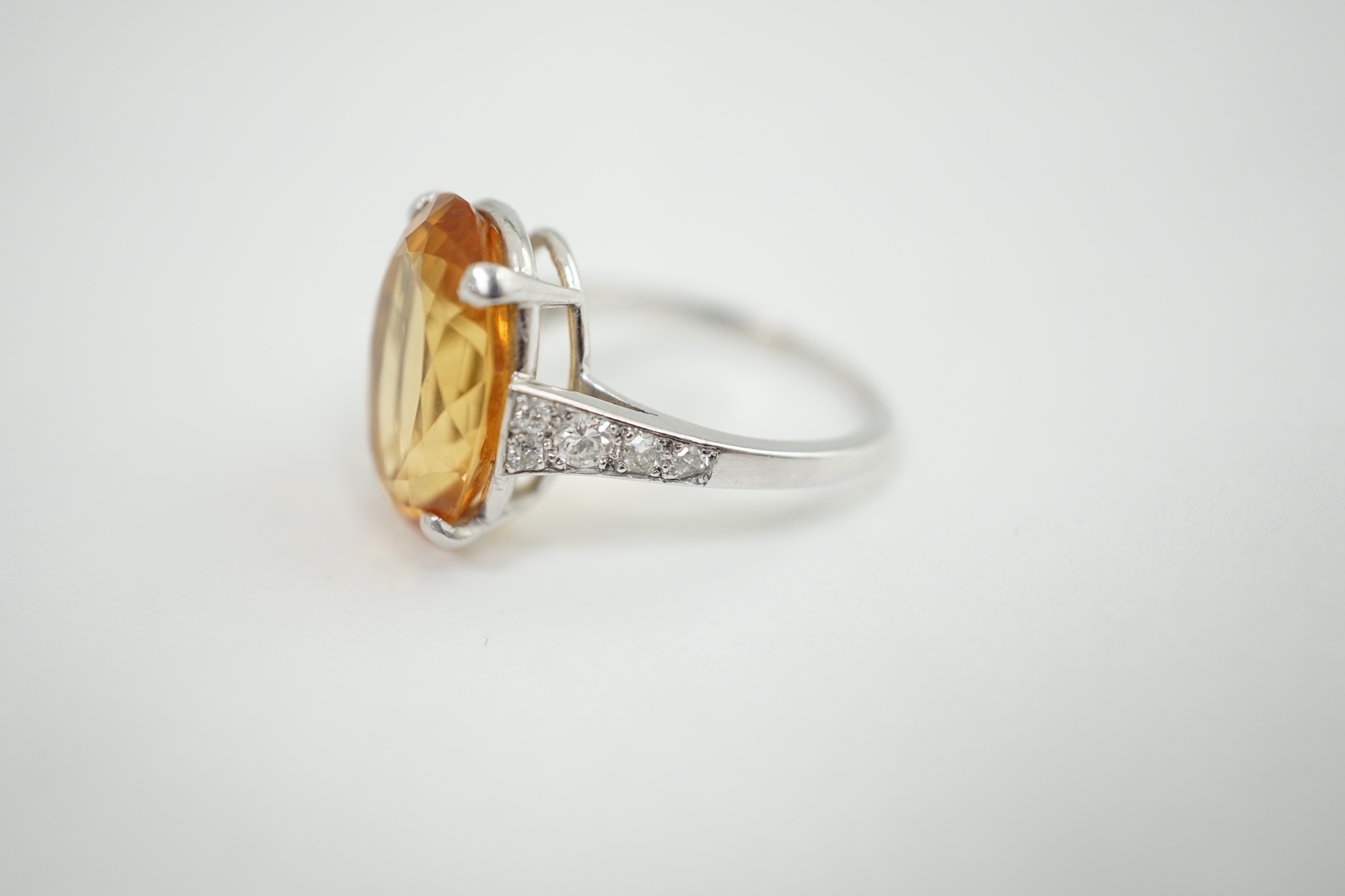 A 1940's platinum? and single stone oval cut imperial? topaz set dress ring, with ten stone graduated round cut diamond set shoulders